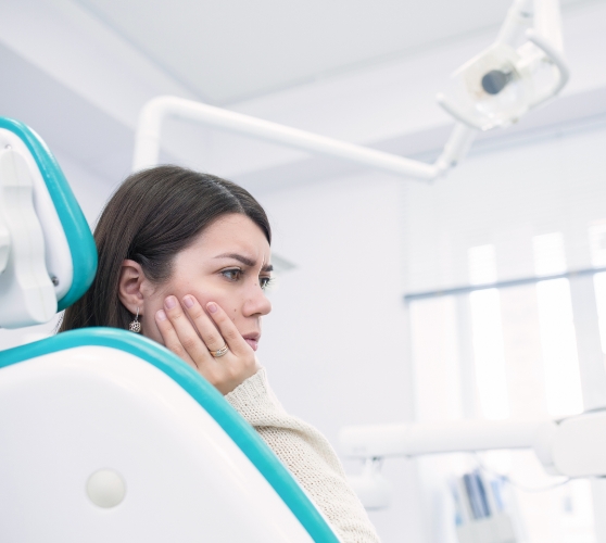 Woman in dental chair holding her cheek in pain