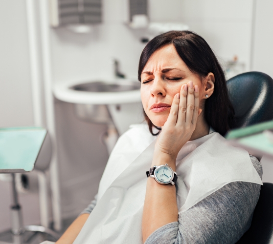 Woman in dental chair wincing and holding her cheek