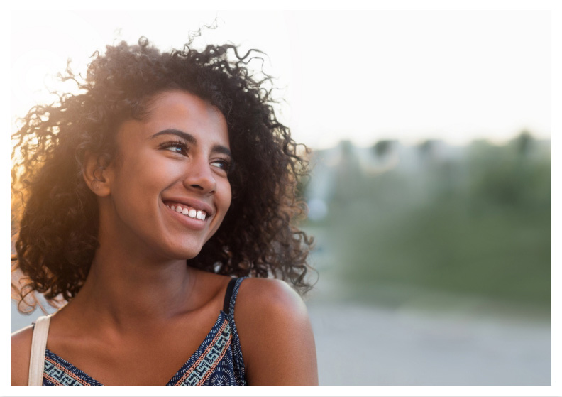 Woman with curly hair smiling outdoors and looking off into the distance