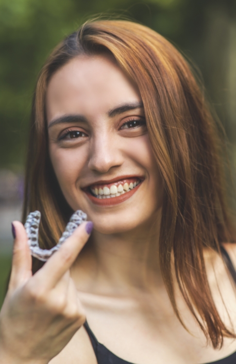 Young woman smiling and holding Invisalign clear aligner in Easton