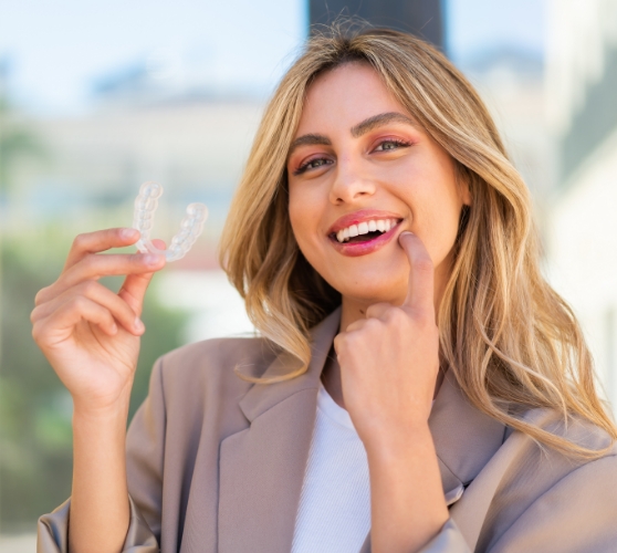 Woman holding an Invisalign aligner and pointing to her smile