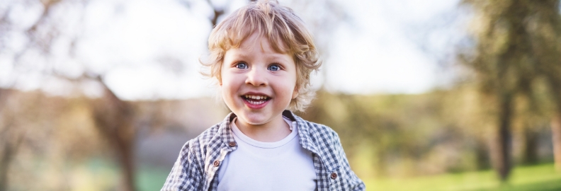 Child with curly blond hair smiling outdoors