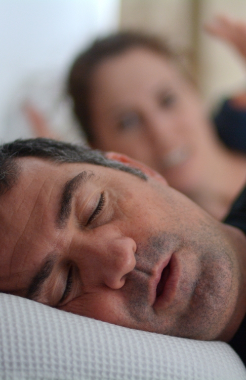 Woman in bed glaring at snoring man next to her who needs sleep apnea treatment